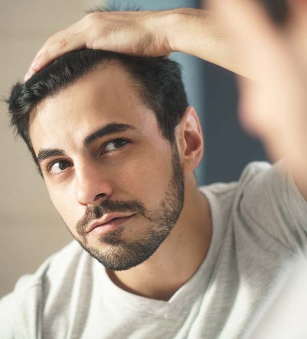 Dark haired man checking out his hair growth in the mirror