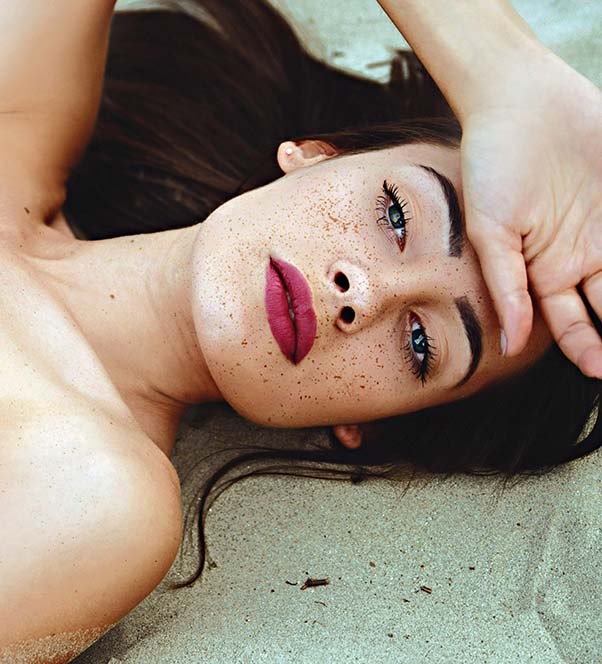 Freckled woman with thick red lips laying down on the beach