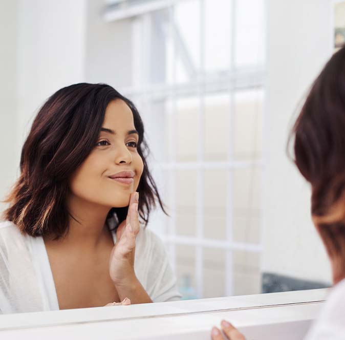 A woman looking in the mirror at her skin after a facial