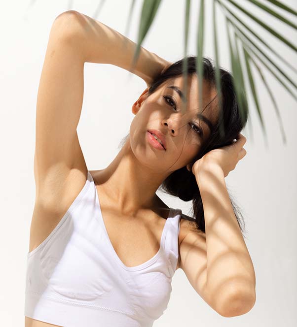 Woman in a white top posing behind a palm leaf