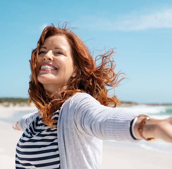 A woman excitedly spinning with her arms out on the beach